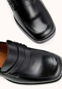 Mocassins en cuir noir au fini brillant, à bout rectangulaire et détail de bandouillère décoratif. Semelle noire unie avec de subtils accents de couture.