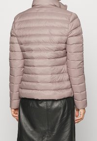 Doudoune mauve clair avec des coutures verticales, un col haut et une coupe ajustée. Portée par-dessus une jupe en cuir noire, mettant en valeur une silhouette moulante.