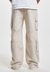 Pantaloni cargo beige con molte tasche laterali, vestibilità rilassata e polsini elastici. Realizzati in tessuto leggero, con dettagli cuciti.