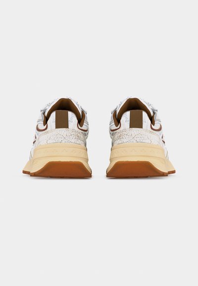 Paire de baskets blanches et beiges avec des accents marron, vues de dos, montrant des semelles intermédiaires texturées et des semelles extérieures en caoutchouc.