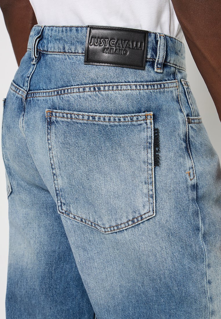 Jean en denim bleu clair avec une poche arrière visible et une étiquette de marque en cuir noir Just Cavalli Milano sur la taille.