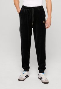 Czarne welurowe spodnie dresowe z elastycznym paskiem, sznurkiem, bocznymi paskami i małym haftowanym logo z przodu.