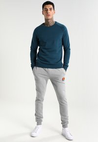 Sudadera azul con cuello redondo y pantalones de chándal grises con un logotipo. Conjunto completado con zapatillas blancas. Textura de tela suave.