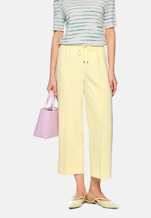 Woman wearing light yellow wide-leg pants, striped short-sleeve top, yellow pointed slingback shoes, holding a lilac handbag.