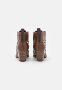 Braune Leder-Stiefeletten mit einer strukturierten Oberfläche, ausgestattet mit einem Blockabsatz, Ziehlaschen und Ziernähten an der Rückseite und den Seiten.