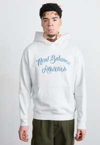 Siva kapuca s prednjo kenguru žepom, koja sadrži plavi tekst "New Balance Athletics". Tkanina izgleda mekano s opuštenim krojem i podesivom kapuljačom.