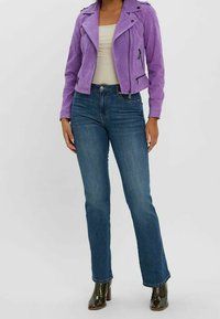 Paarse suède motorjack met ritszakken, gecombineerd met blauwe jeans met rechte pijpen en glanzende laarzen met hak. Soepele textuur en een aansluitend ontwerp.