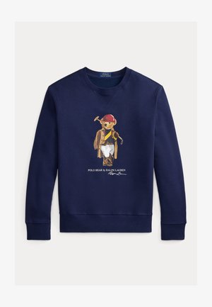 Marineblå genser med en bjørn som har på seg en rød hjelm, brun kåpe, hvite bukser og holder en polo-kølle, med teksten "Polo Bear by Ralph Lauren" under.