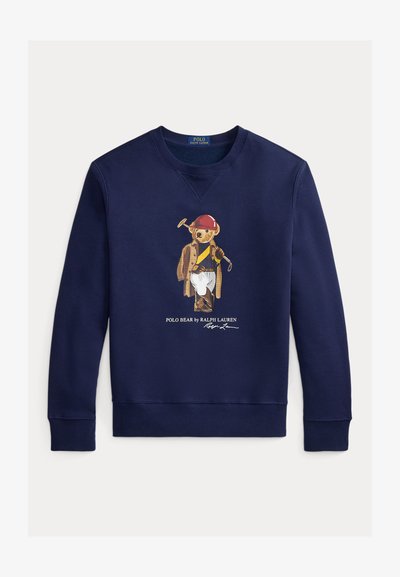 Marineblå genser med en bjørn som har på seg en rød hjelm, brun kåpe, hvite bukser og holder en polo-kølle, med teksten "Polo Bear by Ralph Lauren" under.