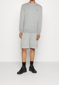 Ljust grå sweatshirt med rund halsringning, sidstygnsdetaljer, matchad med ljusgrå shorts och svarta sneakers.