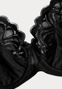 Zwarte kanten beha met geschulpte randen, ingewikkelde mesh- en stippenpatronen, een glad satijnen voering en een klein strikje in het midden.