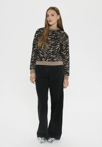 Suéter de manga larga en estampado animal negro y beige, combinado con jeans de pierna ancha negros y zapatos metálicos plateados. Textura de punto plano.