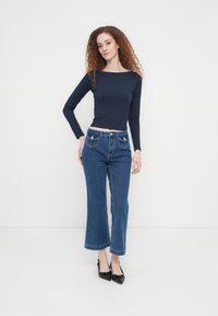 Θαλασσί μακρυμάνικη εφαρμοστή μπλούζα σε συνδυασμό με μπλε τζιν ψηλόμεσο παντελόνι με φαρδιά πόδια και μπροστινές τσέπες. Μαύρα παπούτσια με τακούνι ολοκληρώνουν την εμφάνιση.