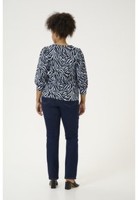 Zwart en lichtblauw zebra-print blouse met puffed mouwen, gecombineerd met donkerblauwe slim-fit jeans en zwarte blokhakken.