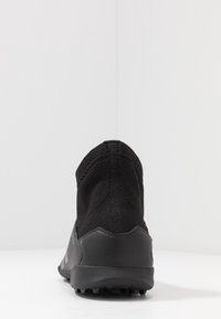 Musta urheilukenkä, jossa on korkea, joustava neulosvarsi ja teksturoitu kumipohja. Ei näkyvää brändäystä, minimalistinen muotoilu takasaumalla.