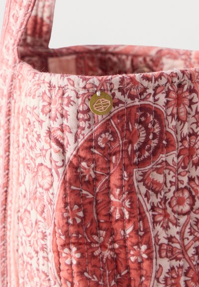 Sac en tissu matelassé à motif floral rose et rouge avec des coutures verticales et un petit charme rond en or près du bord supérieur.