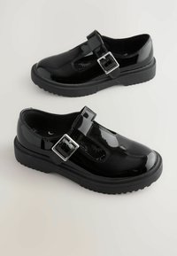 Chaussures en cuir verni noir avec un design à sangle en T, dotées d'une boucle en argent, d'une épaisse semelle en caoutchouc et de surpiqûres décoratives sur l'empeigne.
