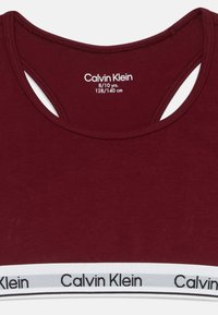 Sutien sport burgund cu decolteu rotund, design racerback și bandă elastică albă cu logo-ul "Calvin Klein". Mărimea 8/10 ani.