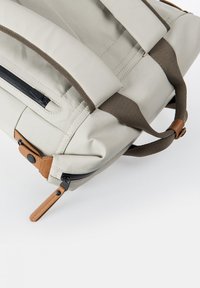 Borsa beige chiaro con manici marrone scuro, dotata di una tasca con zip e dettagli in pelle. Design angolare con cuciture visibili.