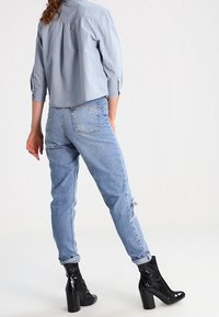 Ljusblå prickig skjorta i cropped stil; högmidjade, slitna ljusblå jeans; blanka svarta ankelskor med klumpig klack.