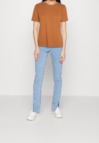 Hnědé žebrované tričko s krátkým rukávem v kombinaci s světle modrými úzkými džínami s bočními rozparky. Obuv tvoří světle zbarvené tenisky.