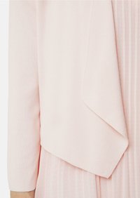 Helle rosa Sweater aus einem weichen, strukturierten Stoff. Verfügt über eine drapierte Front und dreiviertellange Ärmel, die über einem gefältelten Kleid getragen werden.