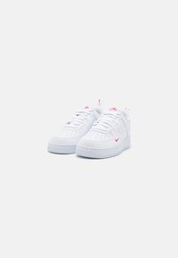 Sneaker in pelle bianca con superficie testurizzata, perforazioni sulla punta, dettagli rossi e suola in gomma. Presentano lacci rotondi e dettagli del logo.