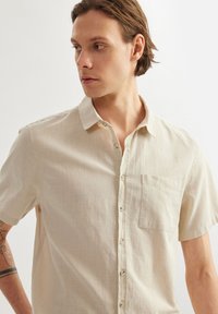Lichtbeige linnen overhemd met korte mouwen, een button-down kraag, een voorzak en een textuurafwerking, voorzien van natuurlijk gekleurde knopen.