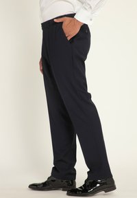Pantaloni da abito blu navy con frontale piatto, due tasche laterali e vestibilità su misura. Il materiale sembra liscio; indossati con scarpe nere lucide.