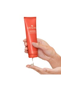 Origins YOUTHTOPIA, oranssin väriin kuuluva puristettava putki, vapauttaa kevyttä voidetta kädelle. Pakkaus sisältää valkoista tekstiä ja logon ylhäällä.