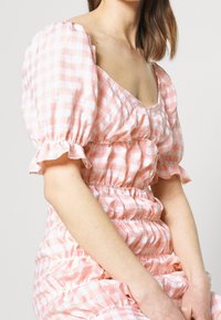 Abito rosa a quadretti con maniche a sbuffo, dettagli arricciati e vita elastica; tessuto leggero con una consistenza morbida.