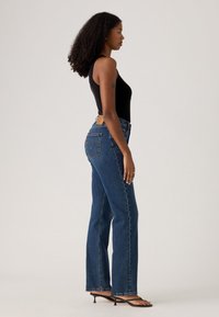 Høyt liv blå denimjeans med rett ben, fem-lomme-design og et lærmerke bak. Glatt tekstur med subtil falming.