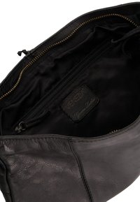 Interiér černé kožené tašky s kapsou na zip a štítkem s nápisem "Venezia." Měkká textura a nestrukturovaný tvar pro všestrannost.