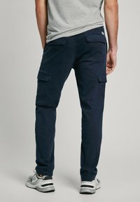 Mørkeblå cargo bukser lavet af bomuld, med flere lommer, lige pasform og en robust talje, parret med grå sneakers.