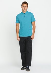 Türkises Polo-Shirt mit kurzen Ärmeln und einer Knopfleiste mit drei Knöpfen, kombiniert mit schwarzen Hosen und dunklen Sneakern. Glattes Material, gerade Passform.
