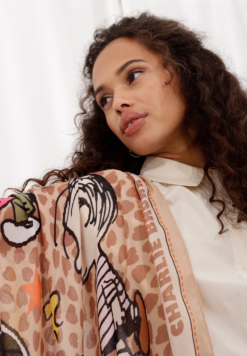 Foulard en soie affichant un motif léopard beige et des personnages illustrés en noir et en couleur. Texte "CHARLIE BROWN" le long du bord. Texture lisse.