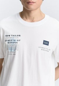 Hvid bomulds t-shirt med grafiske designs i blå og sort, inklusive teksten "TOM TAILOR" og "STREETS OF HAVANA". Klassisk rund hals.