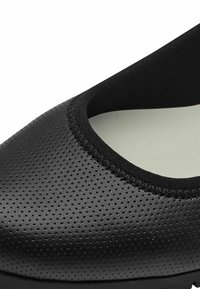 Black perforated shoe with a rounded toe and elasticized fabric collar. Smooth inner lining, minimalistic design, and sturdy sole.
