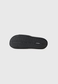 Semelle de chaussure noire avec une surface en caoutchouc texturé, présentant un motif de semelle pour l'adhérence et une étiquette de marque positionnée près du talon.