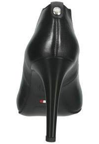 Black high-heeled shoe with a smooth leather texture and pointed toe. Features a decorative button detail at the back near the heel.