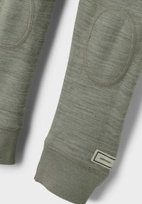 Grön långärmad skjorta med texturerad tyg, med armbågslappar och ribbade ärmslut. Etikett med en minimalistisk design på den nedre ärmen.
