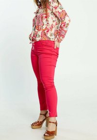 Bright pink slim-fit pants feature a smooth texture and side pockets. Paired with a long-sleeve, floral print blouse and brown heeled sandals.