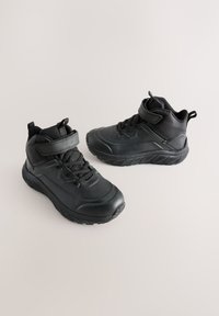 Čierne členkové topánky s textúrovanou gumovou podrážkou, polstrovaným golierom a suchým zipsom. Majú hladký povrch a čierne šnúrky pre bezpečné upevnenie.