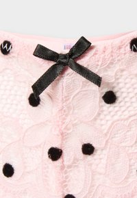 Ανοιχτό ροζ δαντελένιο ύφασμα με ανθικό μοτίβο, μαύρες βελούδινες πουά, και μικρό μαύρο σατέν φιόγκο στο κέντρο της επάνω άκρης.