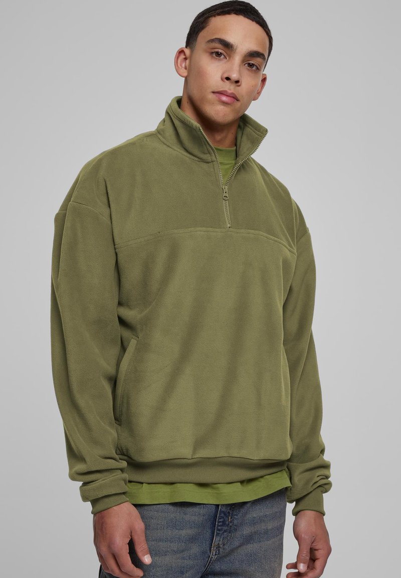 Pullover in pile verde oliva con collo a mezza zip e polsini a coste. Texture morbida, con una cucitura orizzontale sul petto.