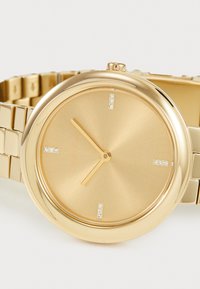 Gold-tone watch with a round face, brushed metallic dial, and three diamond-like markers. Features a linked bracelet and minimalist hands.