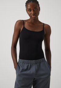Black fitted tank top with thin spaghetti straps, paired with gray elastic waist trousers. Plain design, smooth texture, and minimal detailing.