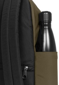 Zaino nero in tessuto con finitura testurizzata, dotato di una tasca laterale contenente una bottiglia d'acqua nera opaca e un dettaglio della cerniera ben visibile.