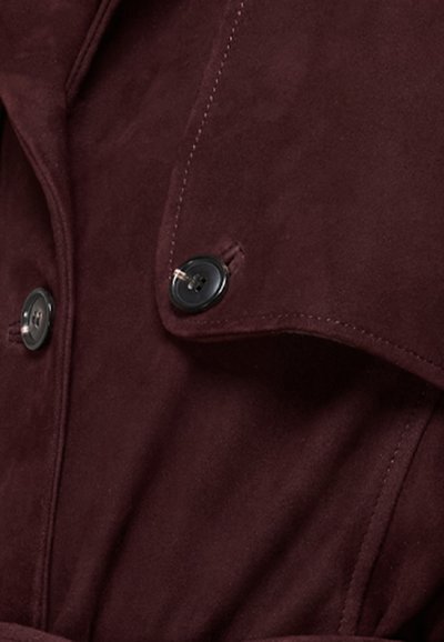 Burgundská zamší trench coat s gombíkovým zapínaním, viditeľným prešívaním a klasickým golierom pre pridanie štruktúry.