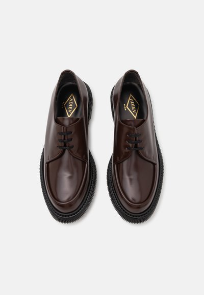 Scarpe in pelle marrone con punta rotonda e design con lacci. La suola in gomma nera a contrasto presenta un motivo testurizzato. Logo dorato sulla soletta.
